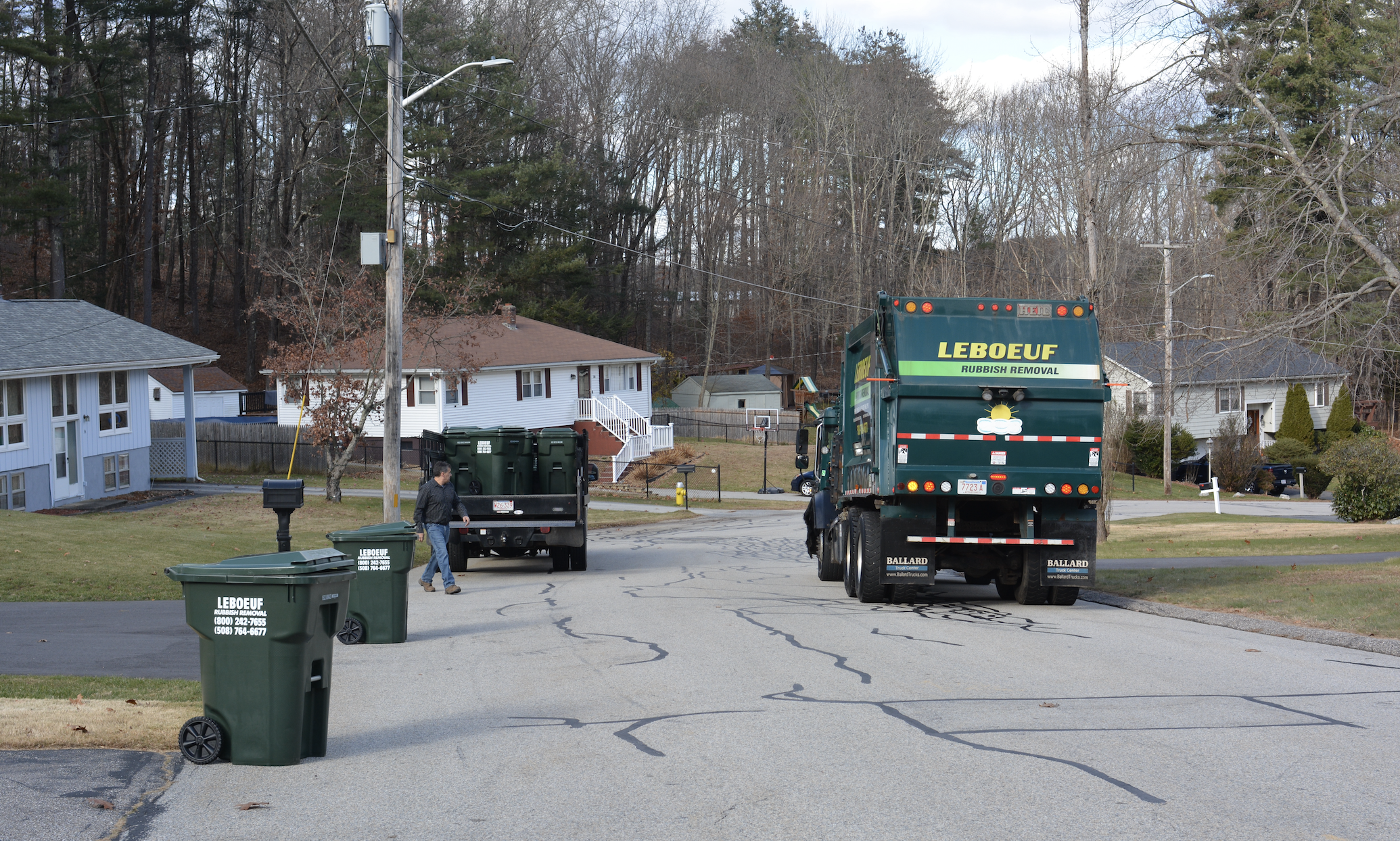 A truck driving past garbage bins set out by the street for pickup.